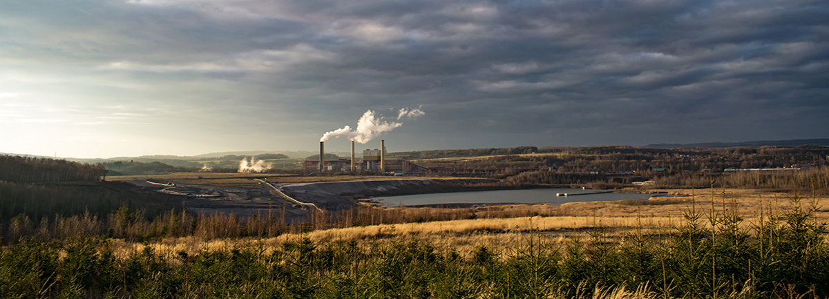 Landscape scene with meadow and lake in the foreground, smokestacks in the background