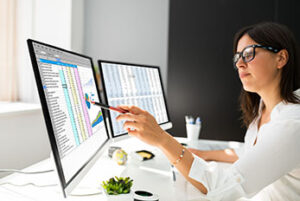 Woman pointing pen at computer screen showing spreadsheet and pie chart