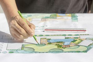 Hand holding green pencil coloring in landscape design
