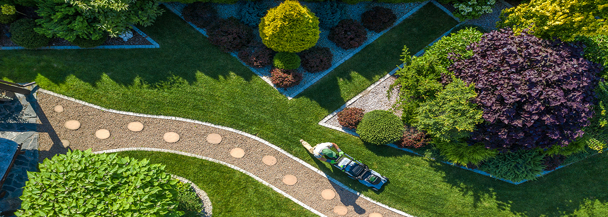 Aerial view of man pushing lawnmower through manicured backyard