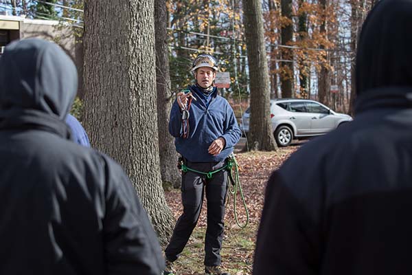 Instructor Mark Chisholm holds up a carabiner as students look on