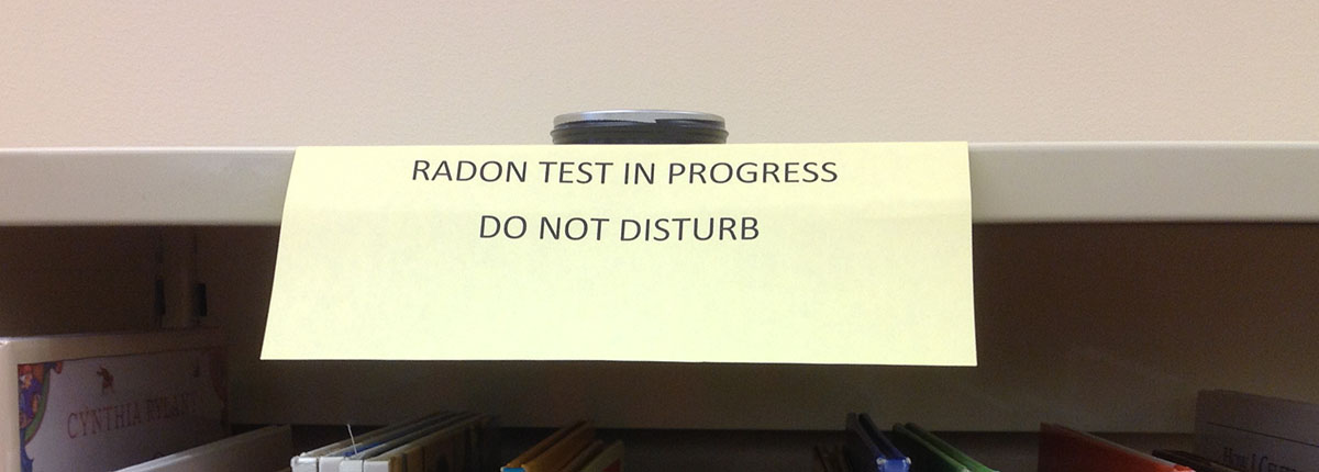 Radon measurement device on shelf in school library with sign saying Radon Test in Progress, Do Not Disturb