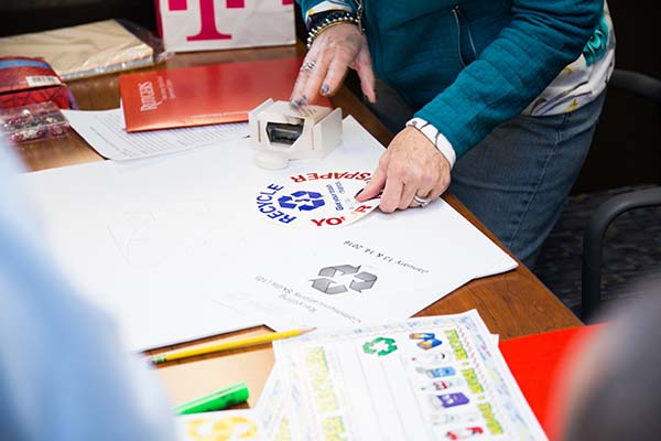 Student places a recycling sticker on a poster during the Improving Your Public Communication Skills class