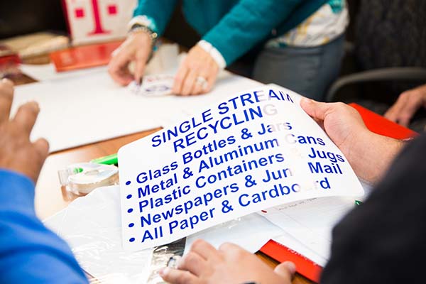 Single stream recycling information sign is held by a student in the Improving Your Public Communication Skills class