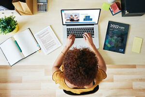 Woman participating in virtual SHRM course on a laptop with SHRM Learning System book on desk next to her