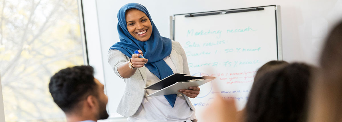 Muslim woman smiling and holding clipboard while giving presentation to colleagues