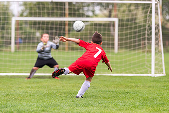 Boy kicking soccer ball toward net on grass field