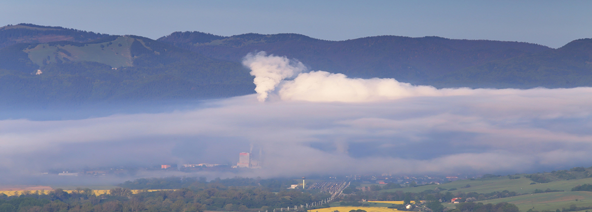 Air pollution emitted from factory smokestack with mountains in the background