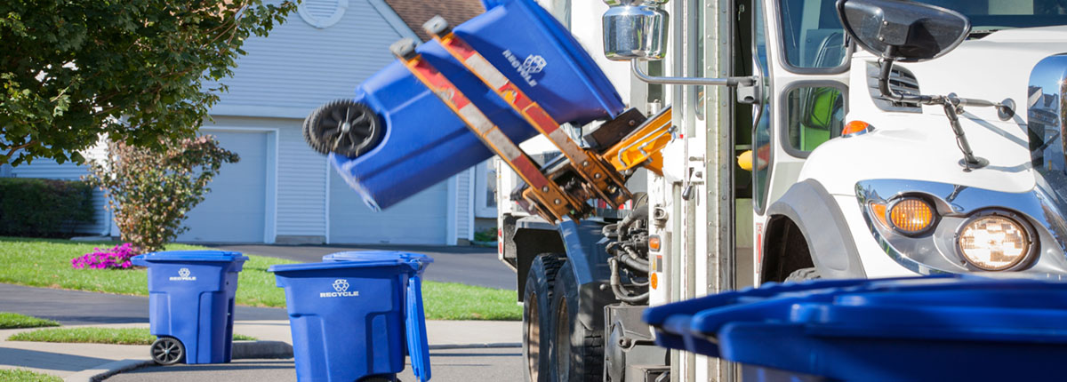 Mechanical arm of recycling truck picking up blue recycling can on residential street